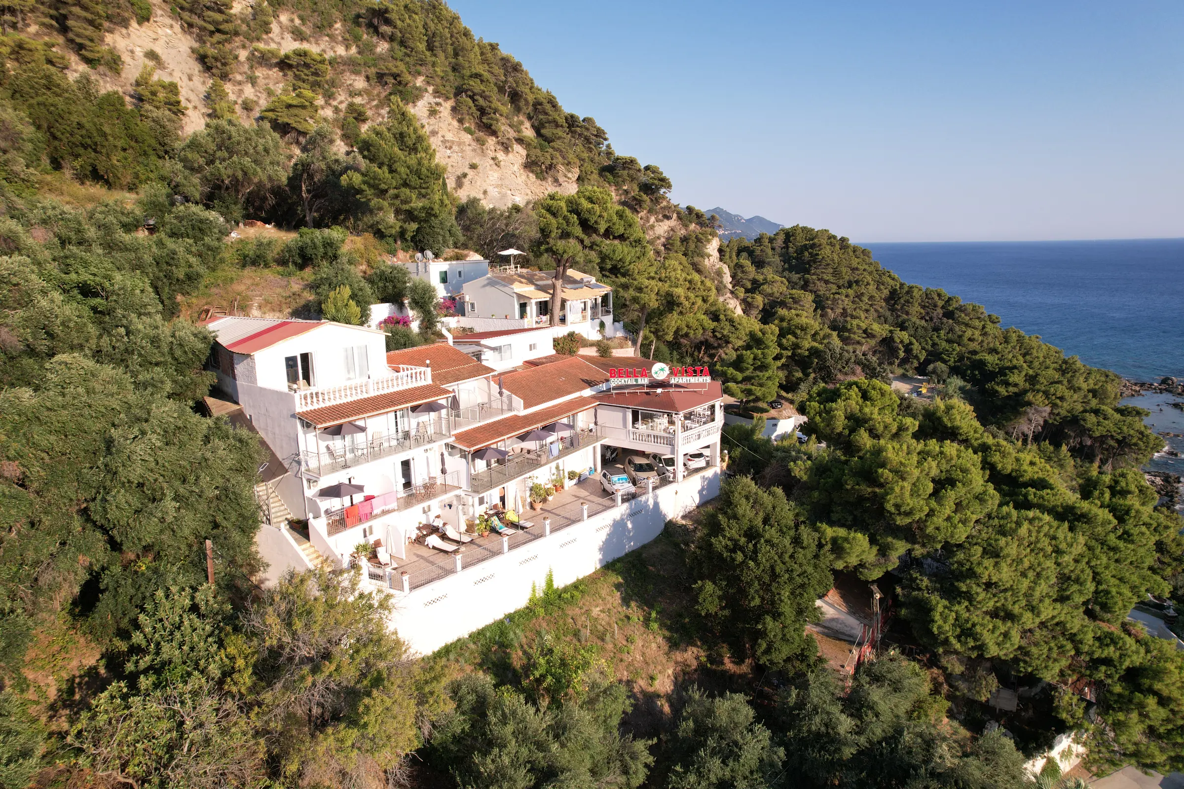 Το Bella Vista από ψηλά: λευκά κτίρια με κεραμιδένιες στέγες στην πράσινη πλαγιά, πάνω από τη θάλασσα